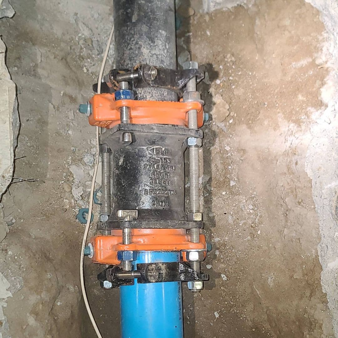 Mechanical coupling joining a black pipe to a blue plastic pipe inside a concrete opening.